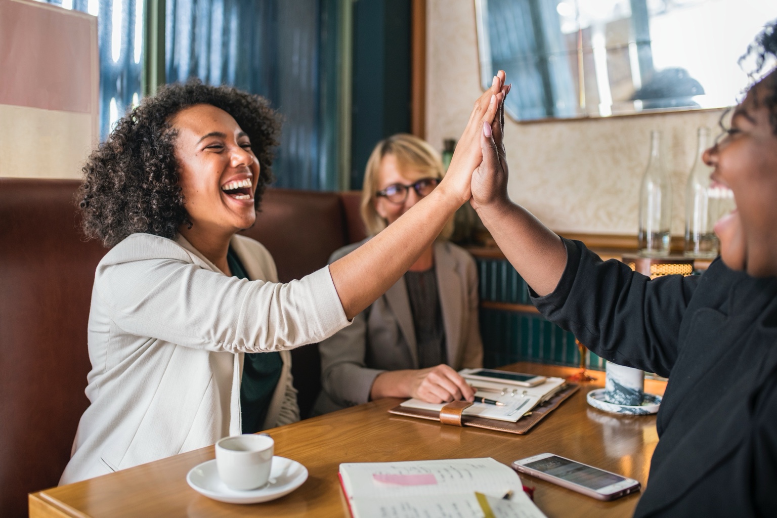 Three colleagues sharing a celebratory high five around a table.